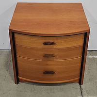 Front view of the teak bedside table showing the three curved drawer fronts with a natural wood finish and wooden handles.