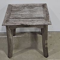 Front view of the teak patio table showing the four legs and slatted top