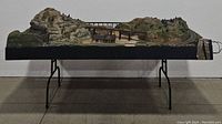 Side view of entire train landscape showing mountain, elevated bridge, and tracks on a stand table.