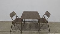Front view of vintage card table flanked by two matching metal folding chairs against a plain wall.