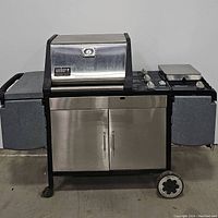 Front view of a Weber Genesis Gold gas grill showing stainless steel doors, black frame, control knobs, and side trays