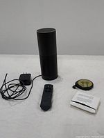 Amazon Echo speaker with remote, charger, earbuds and manual arranged on white surface.