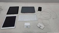 Full lot view showing 2 iPads, Apple wireless keyboard, 2 charging docks, iPod Touch, and iPad holder on a white surface.