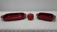 Two rectangular deep red casserole baking dishes flanking a red apple-shaped lidded basket, all placed on a white surface.