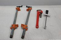 Full lot view showing two woodworking clamps, a red pipe wrench, and a torque wrench on a white surface.