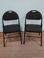 Pair of black metal folding chairs with fabric upholstered padded seats and backs, showing front view.