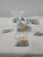 Eight resealable plastic bags each containing various types and sizes of metal peg board hooks laid on a white surface