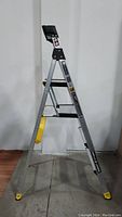 Front side view of the fully extended 5.5ft aluminum Gorilla Ladder showing the dual platforms and structural braces, standing on a concrete floor with a wooden floor border.
