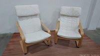 Two IKEA POANG armchairs next to each other showing birch bentwood frame and white cloth cushions on wooden floor.