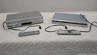 Sony VHS and DVD players side by side with remotes, front view showing unit shape and design.