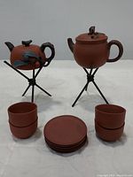 Front view of the two Yixing clay teapots on iron stands, with four cups stacked in twos and six saucers stacked in the middle.