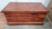 Front view of cedar chest showing wood grain, keyhole, and brass accents on corners.