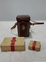 Brown Rollei leather camera case upright next to two Rollei-branded boxes