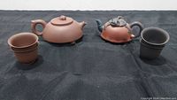 Front view of both teapots and cups on black cloth