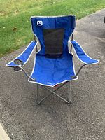Full view of the blue Outbound foldable lawn chair showing armrests, cup holder on right arm, mesh back panel, steel frame, and fabric seat.