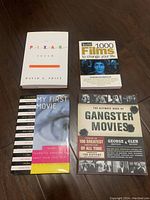 Four film books shown together on a surface, titles visible include The Pixar Touch, 1000 Films To Change Your Life, My First Movie, and The Ultimate Book Of Gangster Movies