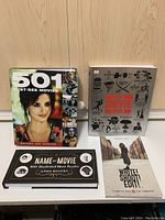 Top view of four movie related books: '501 Must-See Movies', 'The Movie Book', 'Name That Movie' and 'Write! Shoot! Edit!'