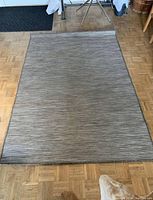 Full view of rectangular gray and white area rug laid flat on wooden parquet floor showing overall color and size.