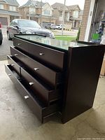 Dark wood dresser with six drawers open showing interior, glass top countertop, visible minor surface wear on top wooden edges.