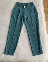 Front view of green high waisted dress pants laid flat, showing tapered legs, zip front, belt loops, and fitted waistband with original tag attached.