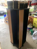 Photo of the full revolving shelving unit showing its height and four vertical panels with wood grain finish on the exterior and black on the interior.