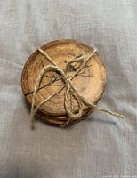 Stack of four round wooden coasters bound with rustic twine, showing natural wood grain and part of bird designs.