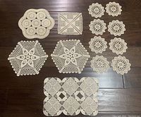Nine total doilies on dark wood floor, six small circular floral lace pattern doilies on right, two hexagonal star crochet pattern doilies on left and one rectangular geometric grid doily at bottom