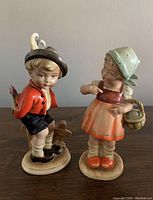 Front view of two porcelain figurines, a boy and a girl, showing their detailed clothing and facial expressions.