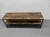 Two wooden top side tables with dark rustic wood finish, black metal frame and mesh lower shelf shown assembled side by side against a white brick wall.