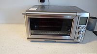 Frontal photo of Breville toaster oven showing digital display, control dials, and stainless steel body.