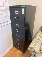 Front view of the black four drawer metal filing cabinet showing all drawers and handles.