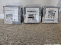 Photo of three packaged furniture protector covers showing front labels and sizes for sofa, loveseat, and chair.