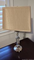 Photo showing one of the matching lamps with a clear glass and metal base, and a rectangular beige fabric shade.