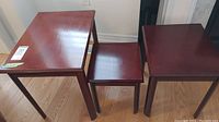 Three reddish-brown wood nesting tables arranged side by side, visible surface scratches on all tables.