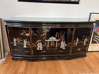 Front view of the black lacquered wood sideboard showing painted Chinese motifs and stone figurine accents.