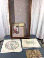 Large wooden rectangular display box with light textured art paper lining and several art paper projects displayed on table.