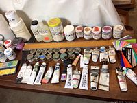 Photo showing assorted tubes and jars of Golden acrylic paint, various colors and sizes, laid out on a surface with color cards visible