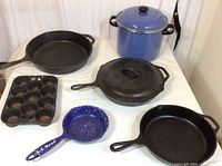 Full overview of all cookware items including cast iron pans, muffin tin, enamel pots and pan on white surface