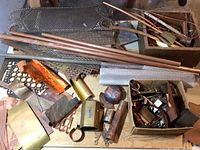 Overview of assorted metal sheets, copper pipes, various scrap metals, and mesh laid out on a surface.