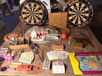 Overview photo of lot showing two round dart boards, backboard, many toys, playing cards, and game pieces on table
