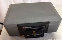 Closed gray textured portable safe with black front handle and key lock, model Sentry 2110.