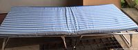 Folded out cot showing blue and white striped fabric surface resting on a metal frame.