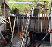 Wide view of assorted long-handled gardening tools including rakes, shovels, axes, and a Black & Decker weed wacker