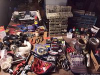 Overview of hardware lot with plumbing fittings, tapes, fasteners, tools, and accessories on table