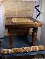 Full view of the rustic Indonesian wood table with the bamboo top panel and a rolled bamboo shade in front.