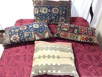 Full view of all four kilim pillows arranged on red patterned cloth showcasing their varying colors and traditional designs.