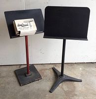 Two music stands visible, one black metal with tripod base and one red metal with wooden square base, both feature black sheet holders.
