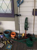Photo of assorted garden tools, pots including ceramic pots in various colors, electric hedge trimmer, and watering can