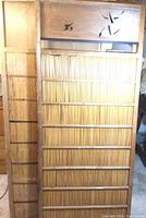 Two bamboo sliding panels leaning against wall: one large with decorative carved top and one smaller plain behind it.