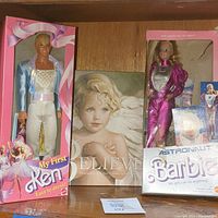 Photo showing the My First Ken doll, Believe poetry book, and Astronaut Barbie doll in their original packaging on a wooden shelf.